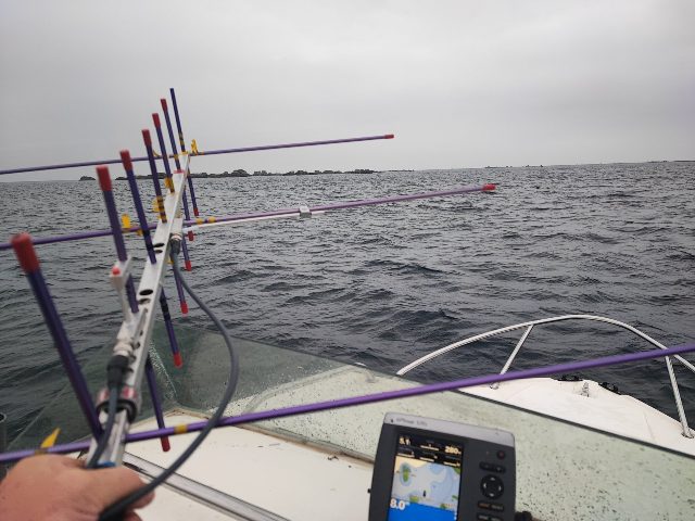 On a boat, the crossed Yagi in hand at the bow, islets in the distance — August 2025